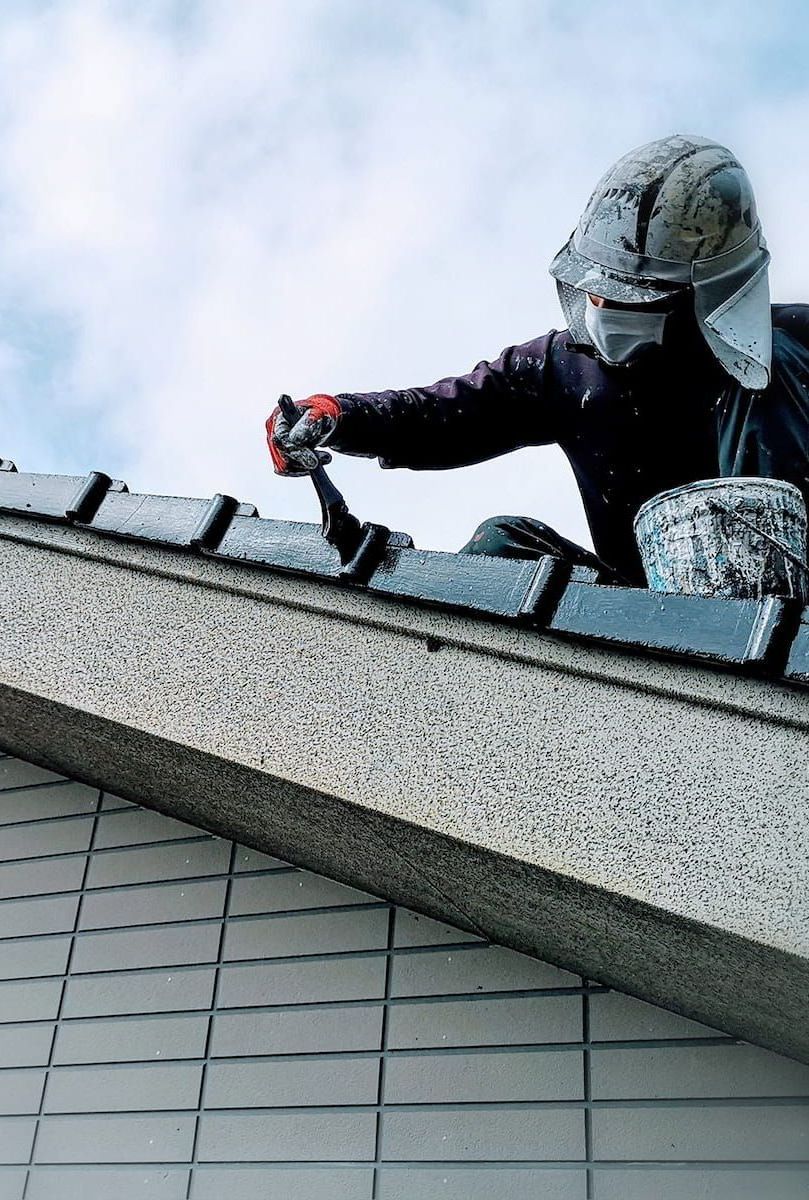 A Man is Painting the Roof of a Building — Roof Restoration Masters In Morisset, NSW