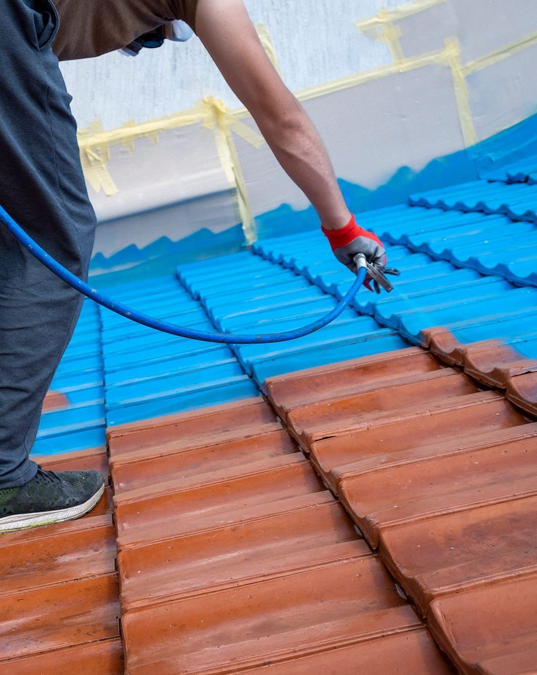 A Man is Spraying Blue Paint on a Tiled Roof — Roof Restoration Masters In Thornton, NSW
