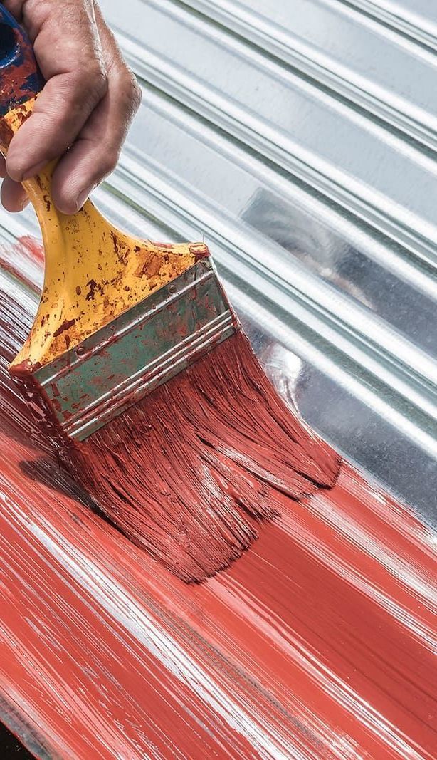 A Person is Painting a Metal Roof With a Brush — Roof Restoration Masters In Charlestown, NSW