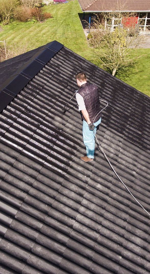 A Man is Spraying a Roof With a Hose — Roof Restoration Masters In Chittaway Bay, NSW