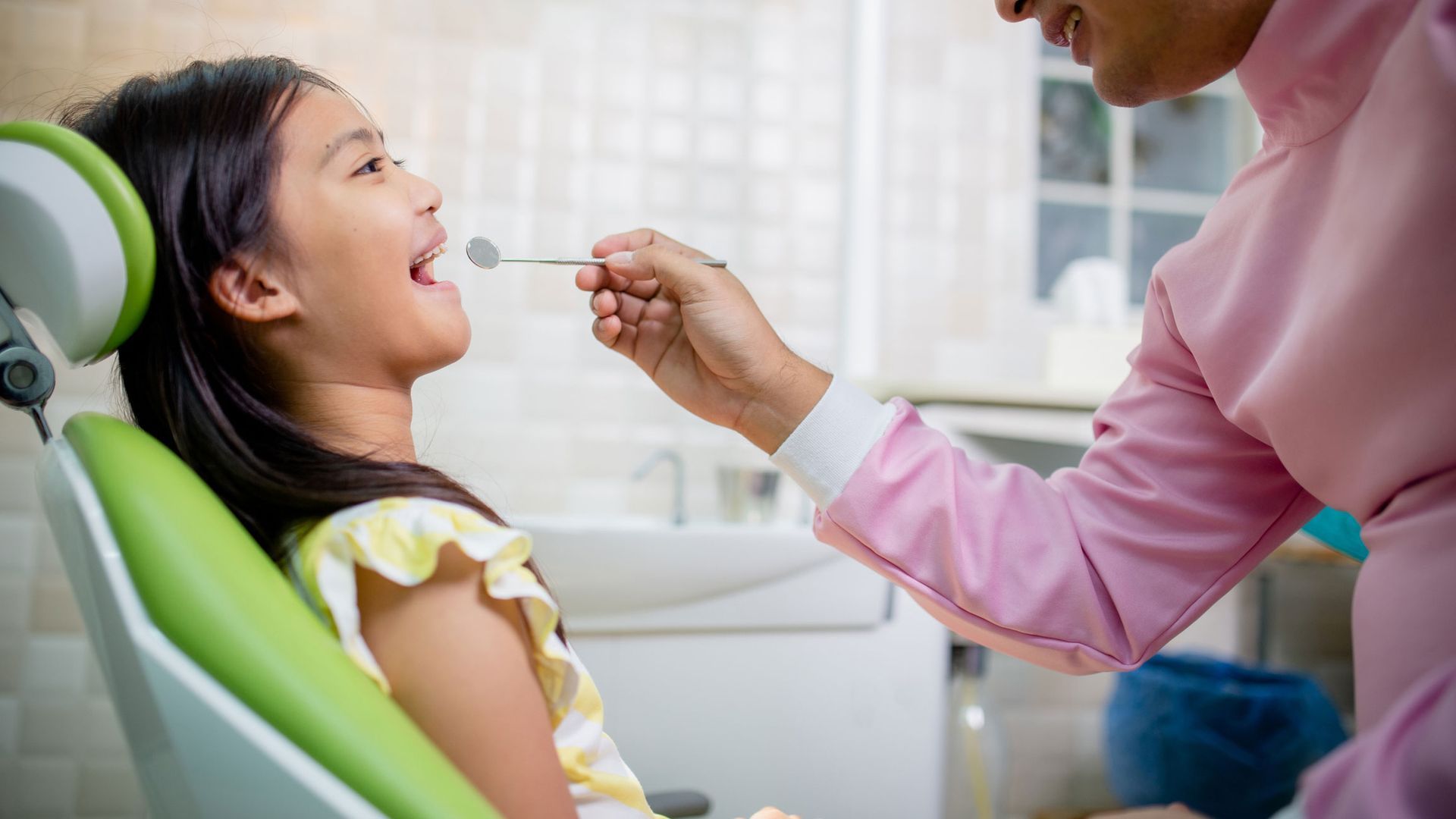 Friendly children's dentist examining a happy child's teeth in a modern dental clinic.