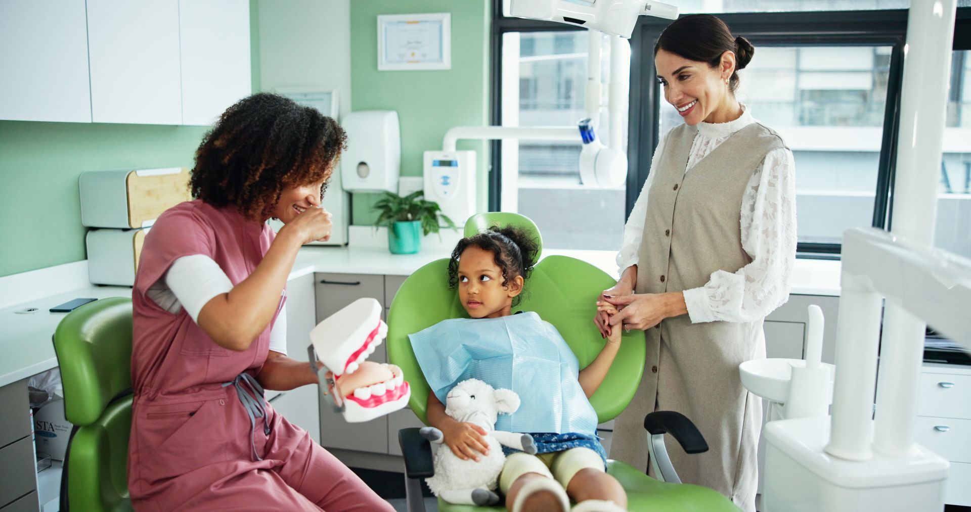 A dentist is teaching a girl how to correctly brush her teeth.