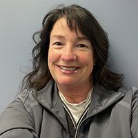 A woman in a gray jacket is smiling for the camera.