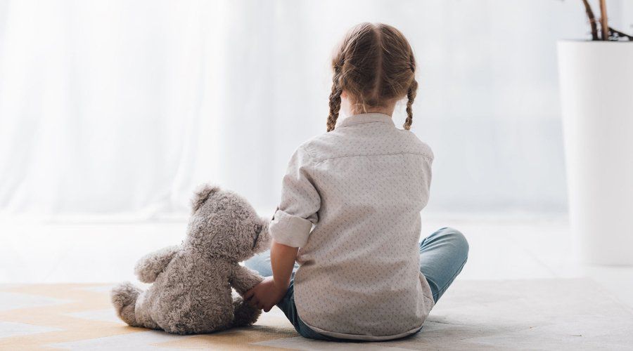 A little girl is sitting on the floor holding a teddy bear.