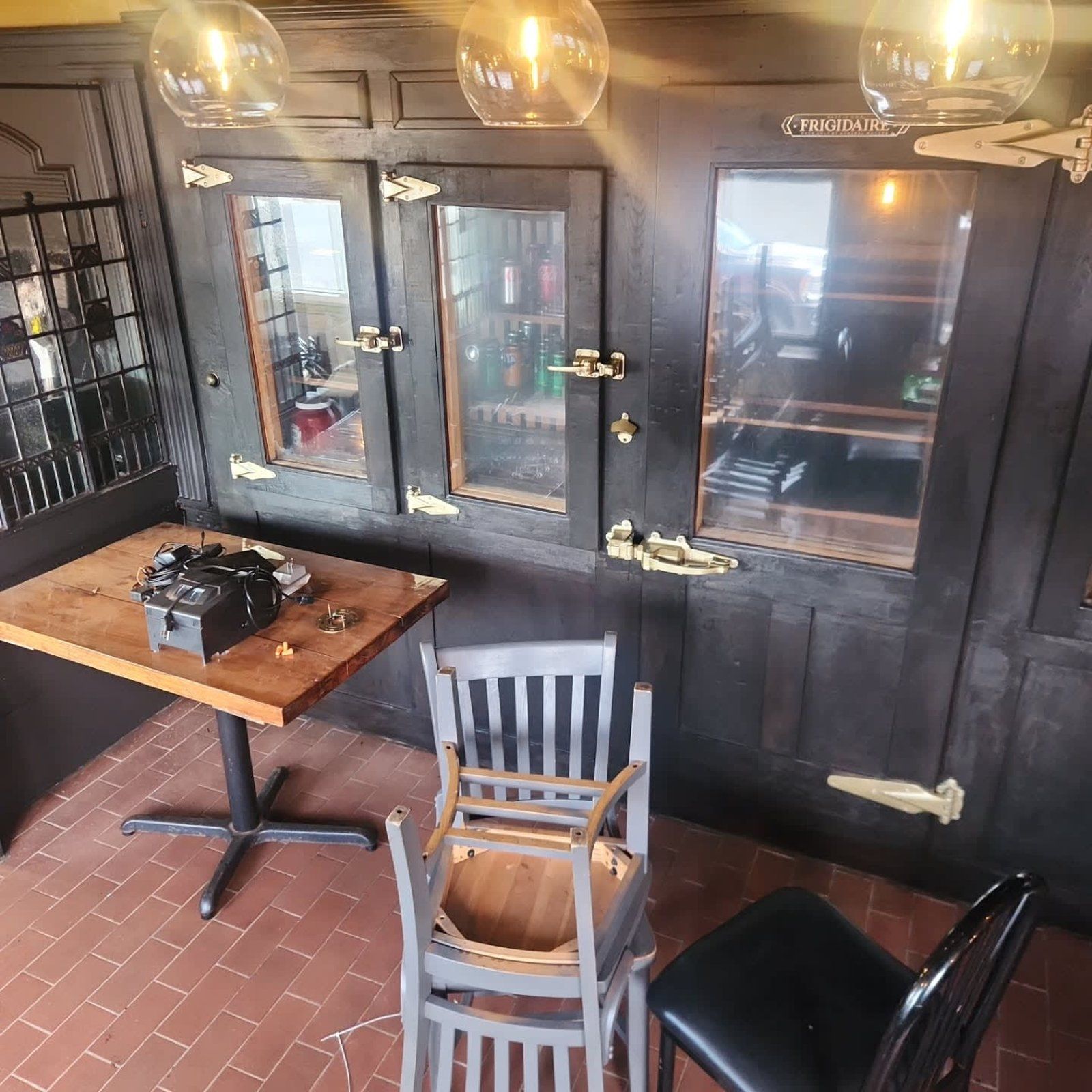 Interior of a bar, showing a table, chairs, cabinets, and hanging lights.