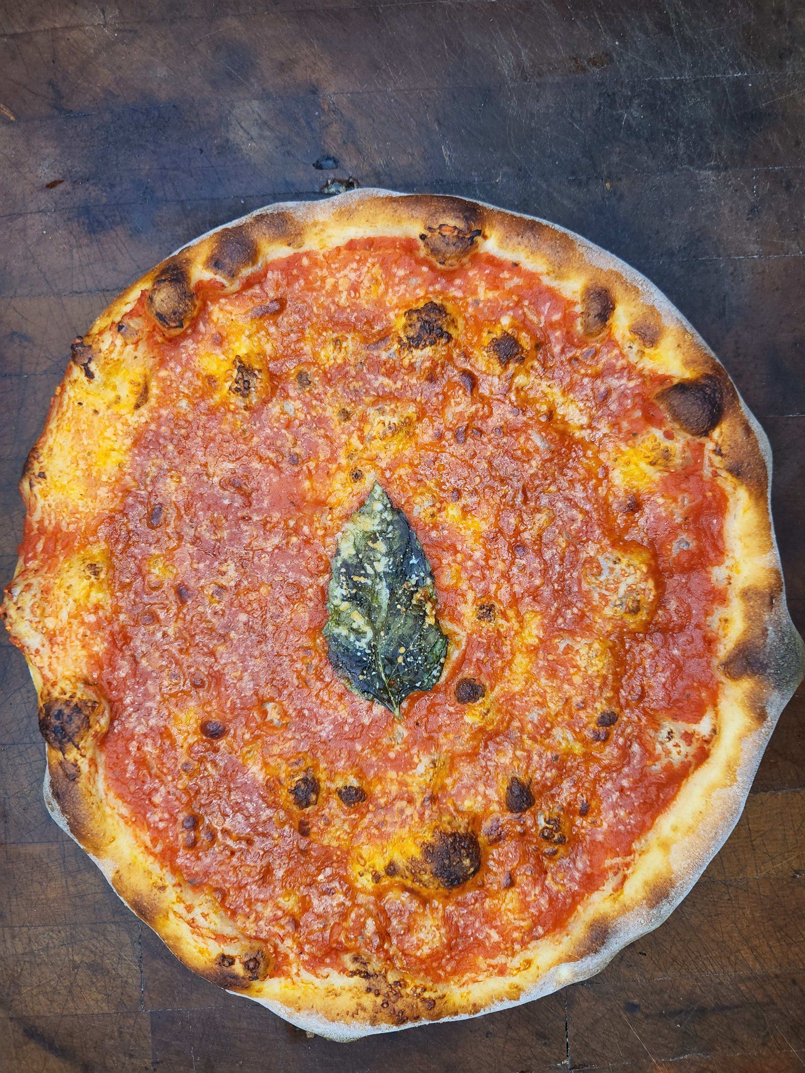 Pizza with red sauce and a basil leaf on a wooden surface.