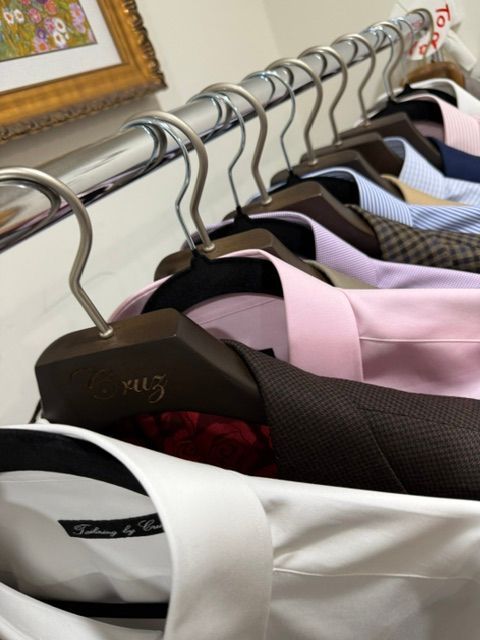 Shirts and suit jackets hanging on a chrome rod in a closet, varying colors.