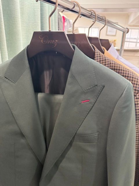 Green suit hanging on a rack with other suits in a tailor shop.