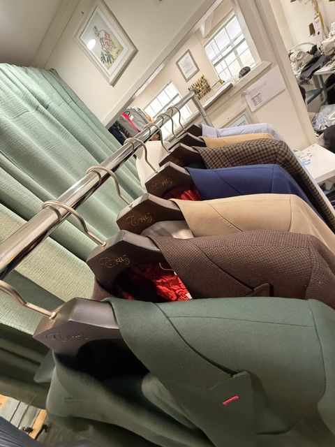 Row of suit jackets in various colors hanging on a rack inside a shop.