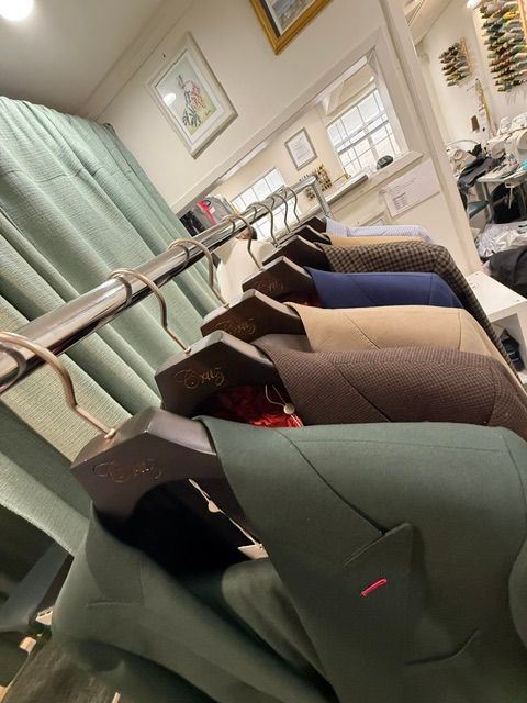 Row of tailored suit jackets in various colors hanging on a clothing rack in a shop.