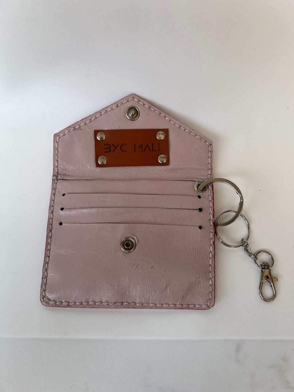 Cartera de piel color rosa pálido con parche marrón, cierre a presión y llavero.