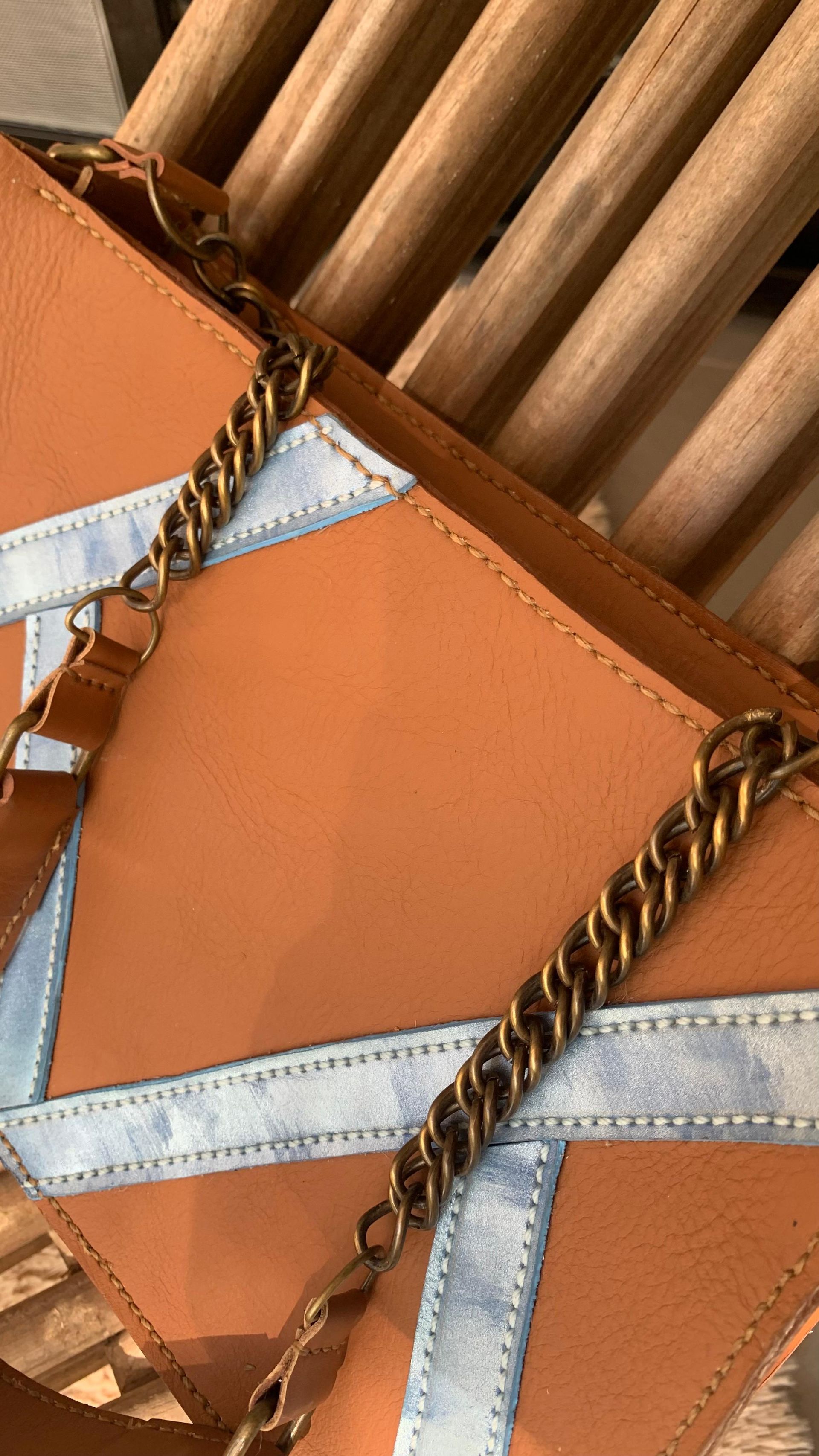 Bolso de piel marrón, abierto para mostrar el interior; costura decorativa azul.