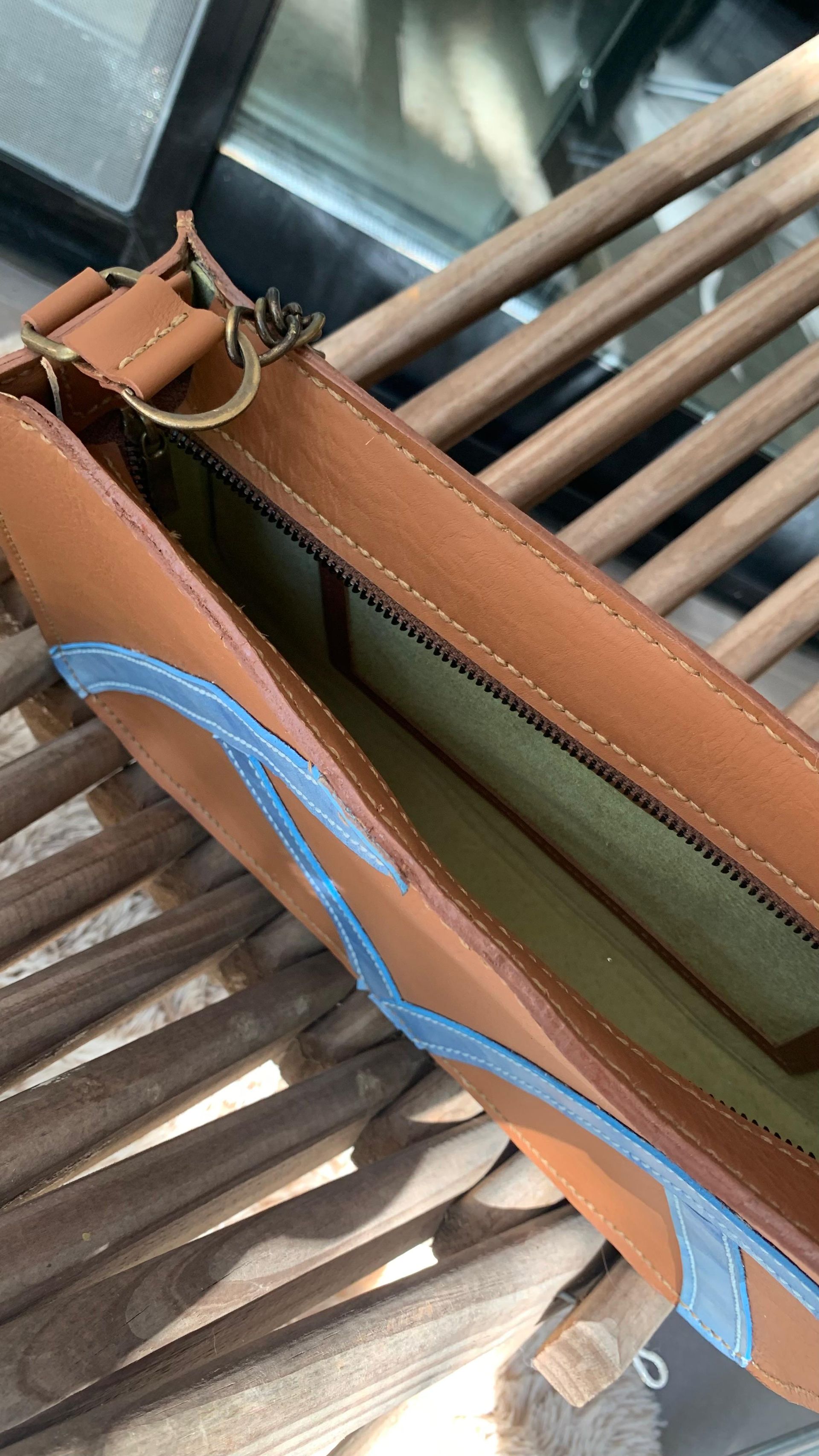 Bolso de piel marrón, abierto para mostrar el interior; costura decorativa azul.