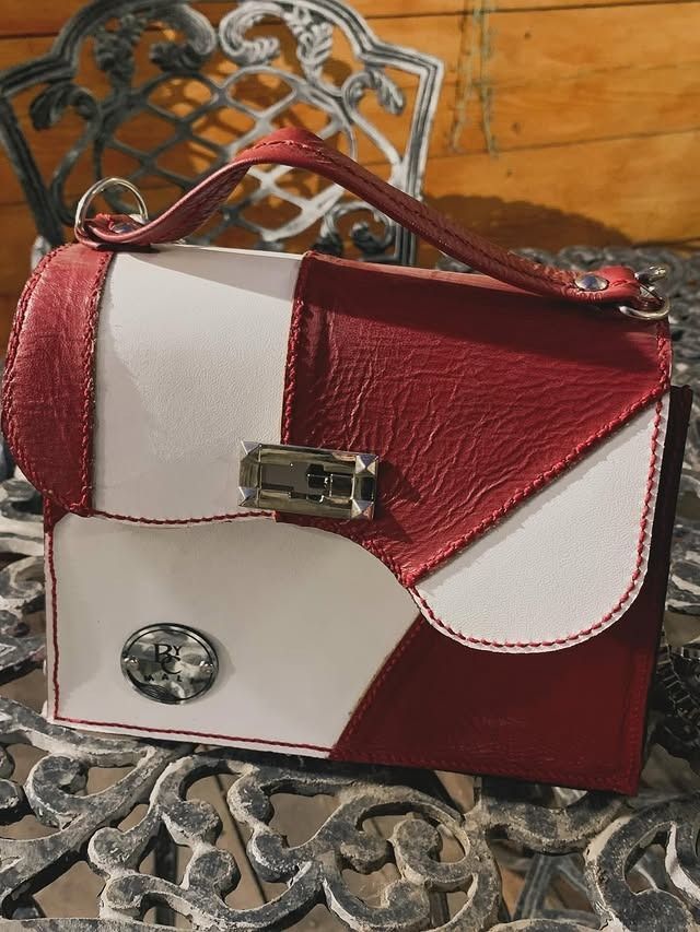 Bolso de mano de piel roja y blanca con asa y cierre plateado sobre mesa decorativa.