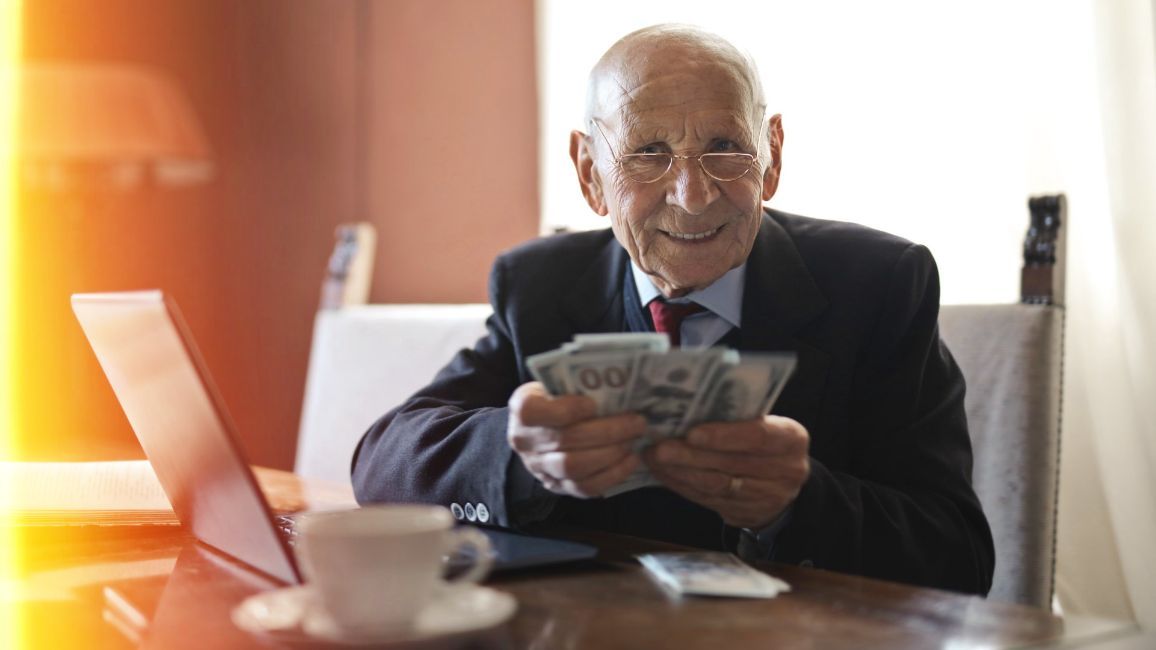 an older man is sitting at a table holding a bunch of money .