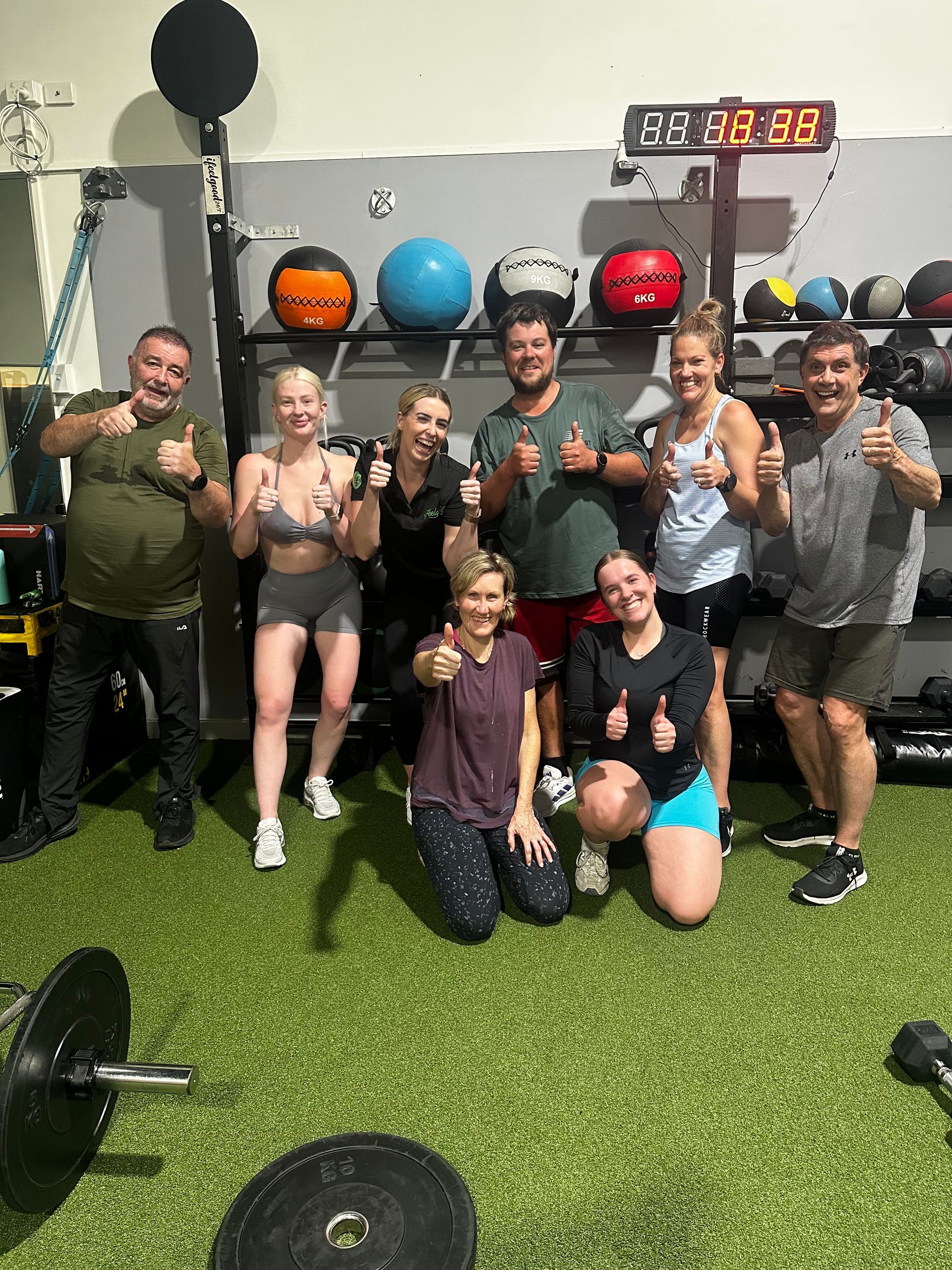 Group posing and smiling for a photo on the green turf after completing their workout β ifeelgood 24/7 Oxenford In Oxenford, QLD