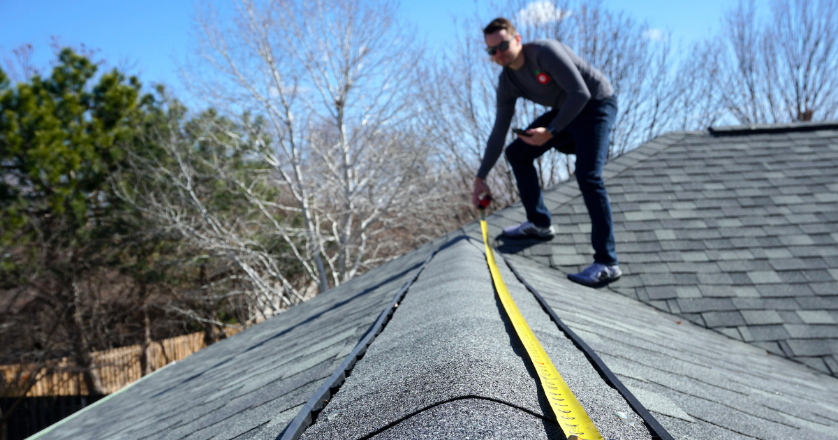 contractor on a home's roof taking measurements.