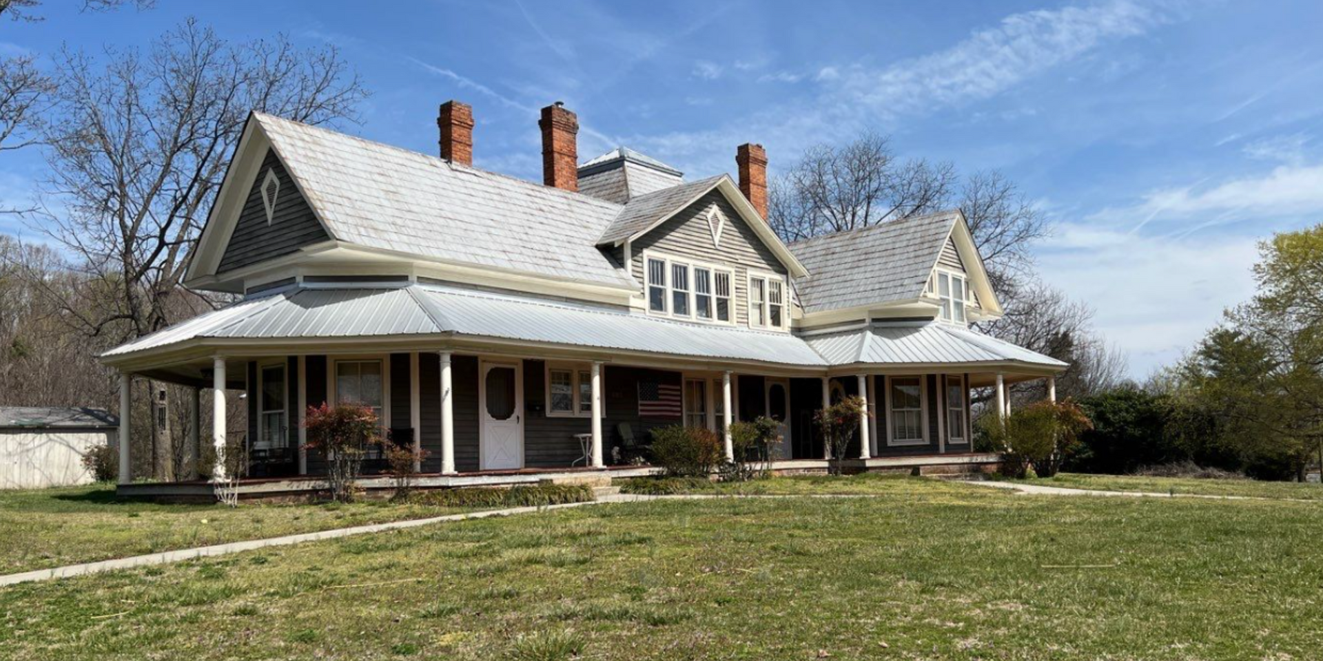 A large house with a large porch is sitting on top of a lush green field.