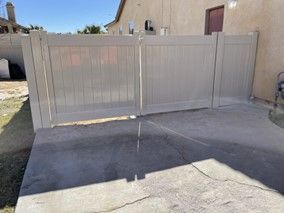 A White Fence Is Sitting on Top of A Concrete Driveway Next to A House — Nuevo, CA — Golden West Fence