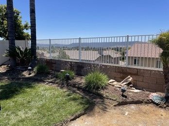 A White Fence Is Surrounding a Brick Wall in A Backyard — Nuevo, CA — Golden West Fence