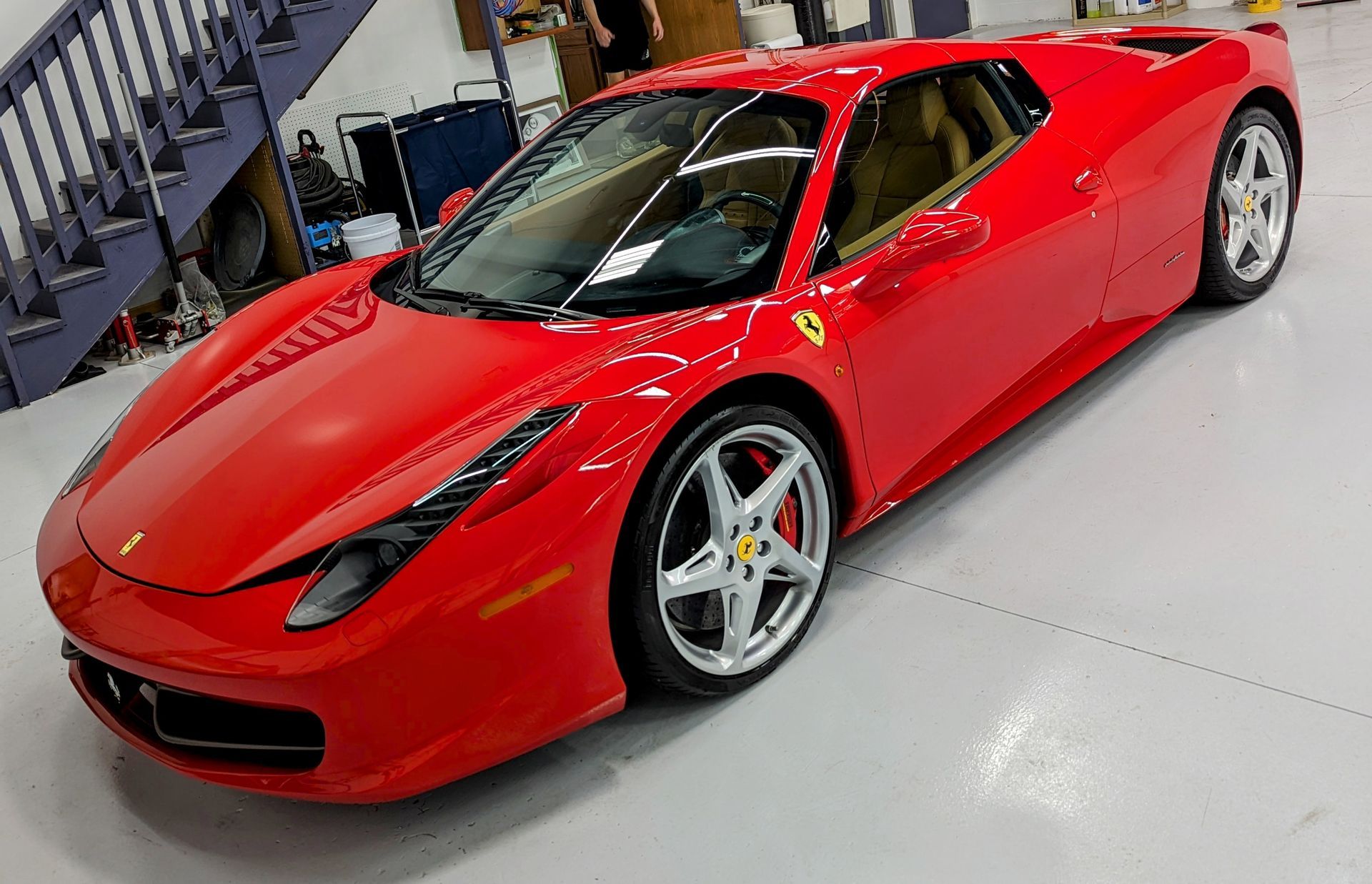 A red ferrari is parked in a garage next to stairs.