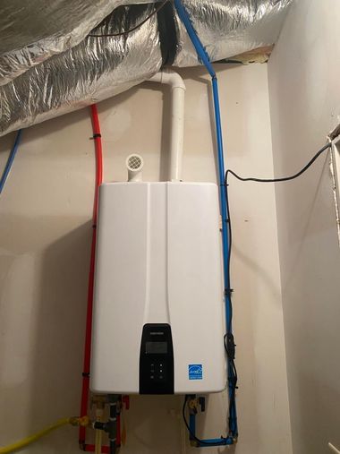 Wall-mounted white boiler with pipes and blue/red cables in a utility room