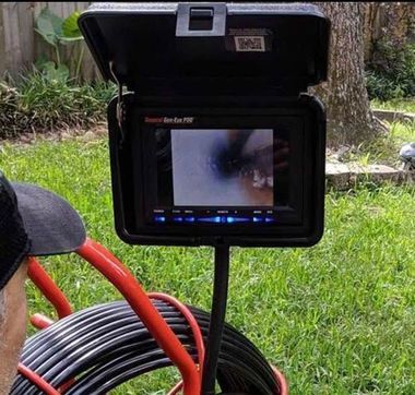 Open field monitor on a black case beside coiled cable in a grassy yard, with a blurred image on the screen