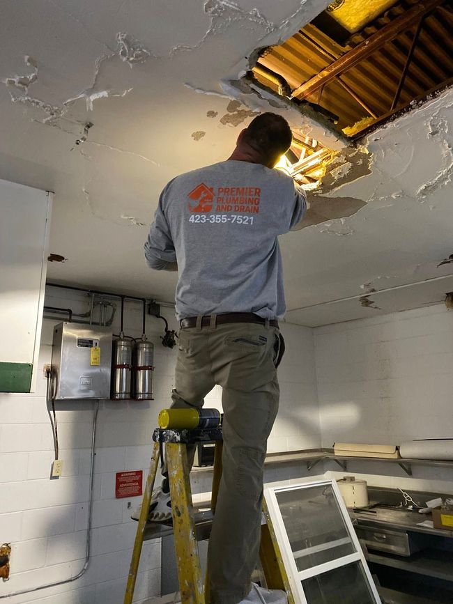 Worker on a ladder repairing a damaged ceiling with exposed insulation in a utility room