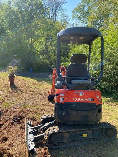 Red Kubota mini excavator on dirt near trees in a wooded area