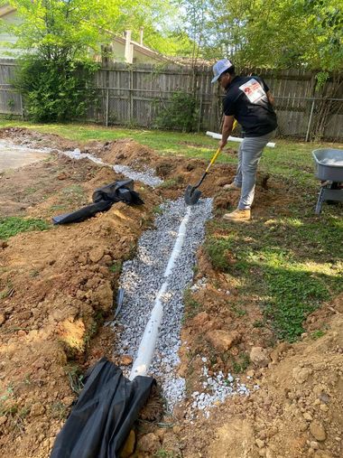 Worker laying white gravel in a trench beside a fence in a yard