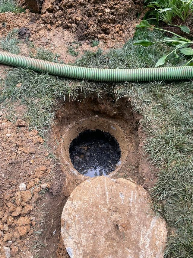 Small dug hole in dirt with a dark opening, a concrete cover below, and a green hose across the top.