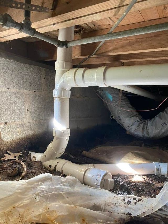 Damaged crawlspace plumbing with a white PVC pipe leaking onto plastic sheeting beneath floor joists
