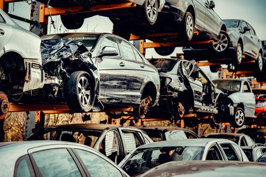 Auto incidentate accatastate in un deposito di rottami, con file di veicoli danneggiati su scaffalature metalliche.