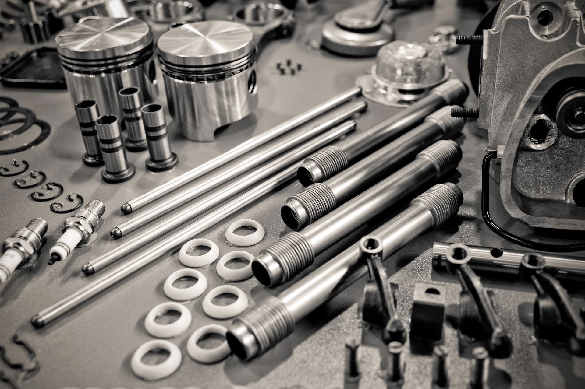 Vari componenti metallici di un motore e attrezzi, tra cui pistoni, bulloni e bielle, sono disposti su un banco da lavoro.