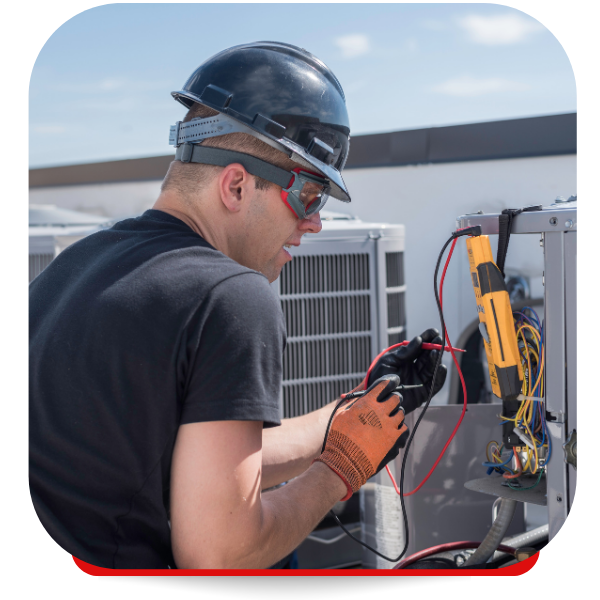 HVAC technician on a rooftop, wearing a hard hat, testing wires with a multimeter.
