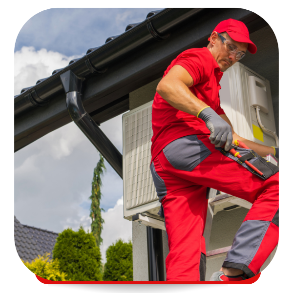 HVAC technician in red jumpsuit and hat, servicing an outdoor unit near a roof and gutter.