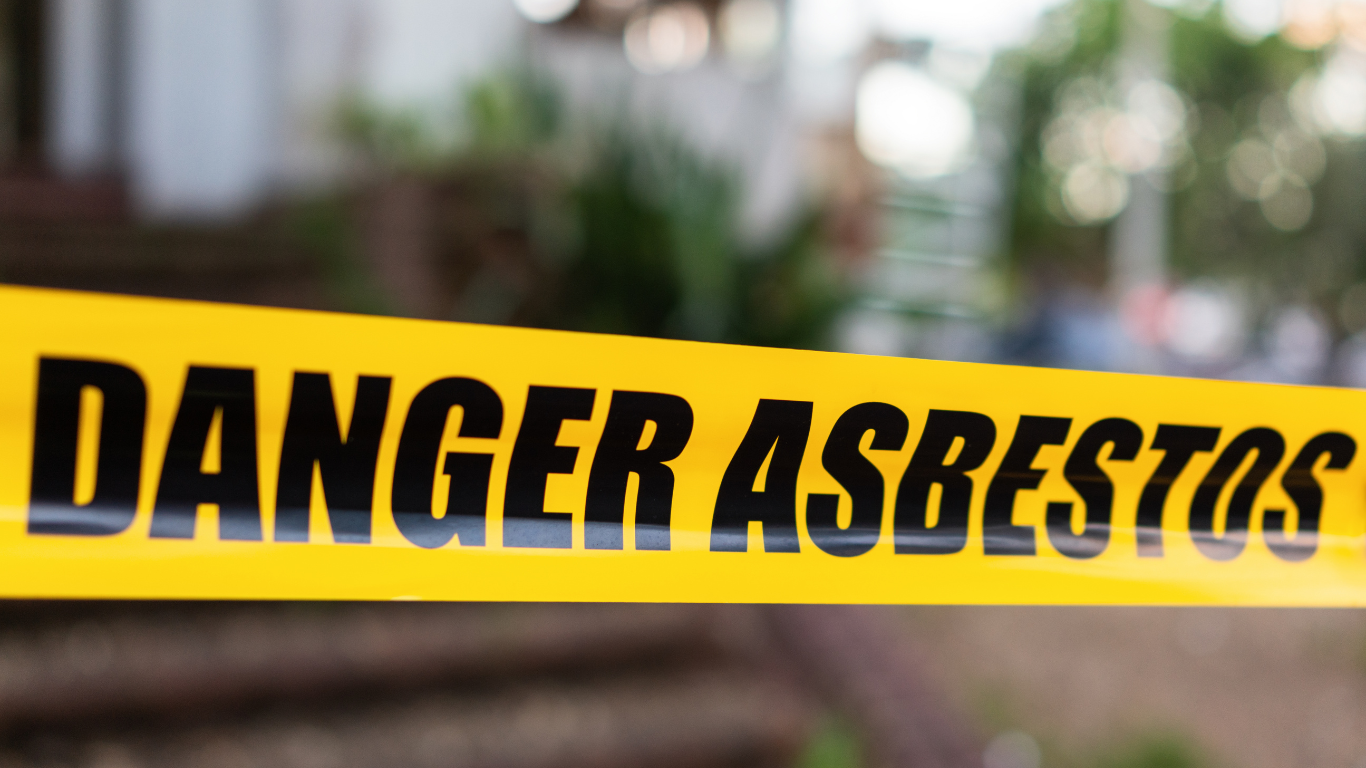 A man wearing a blue protective suit and goggles is standing in front of a brick building.