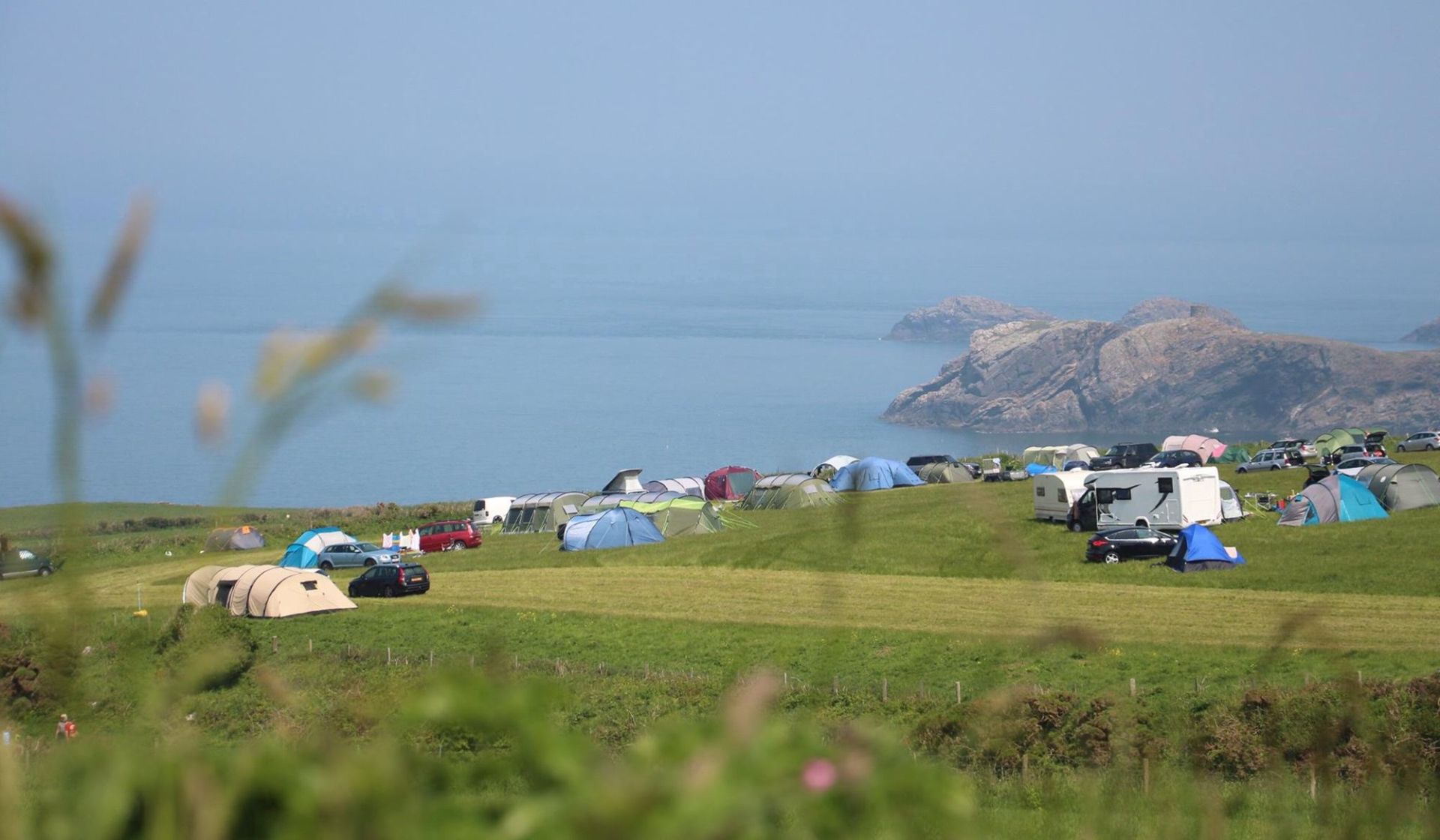 dozens of tents and campervan in front of a sea view