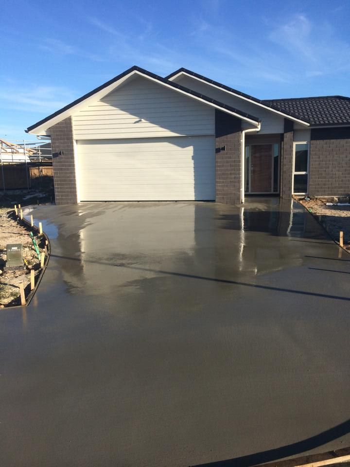 Newly poured concrete driveway in front of a modern house with a white garage door and brick accents.