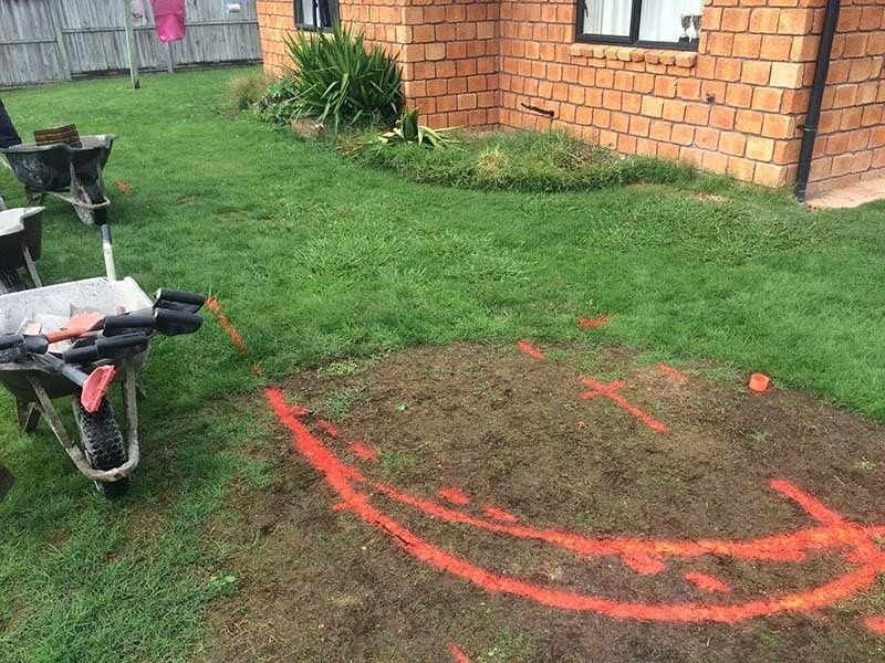 Wheelbarrows near a lawn marked with orange paint, likely for landscaping near a brick building.