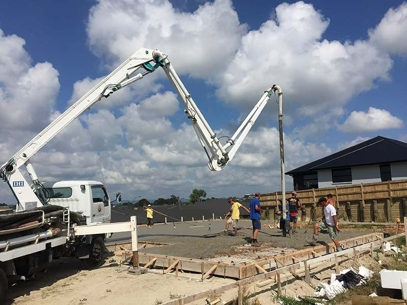 Concrete pump truck pouring concrete into foundation, blue sky. Construction workers smoothing the wet cement.