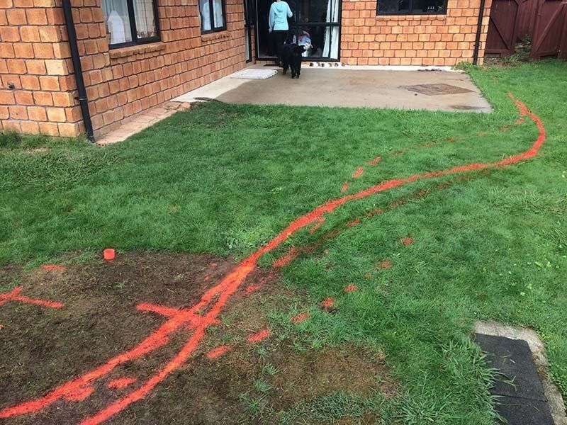 Orange spray paint outlines a curved path across a grassy yard, leading to a brick building.