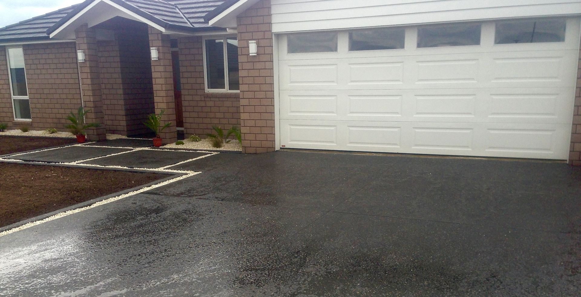 A brick house with a white garage door, dark asphalt driveway, and a landscaped walkway.