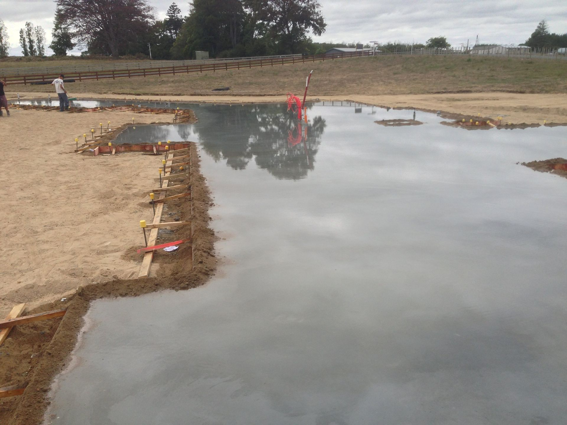 Wet concrete poured in a shallow foundation, surrounded by wooden forms on a construction site.