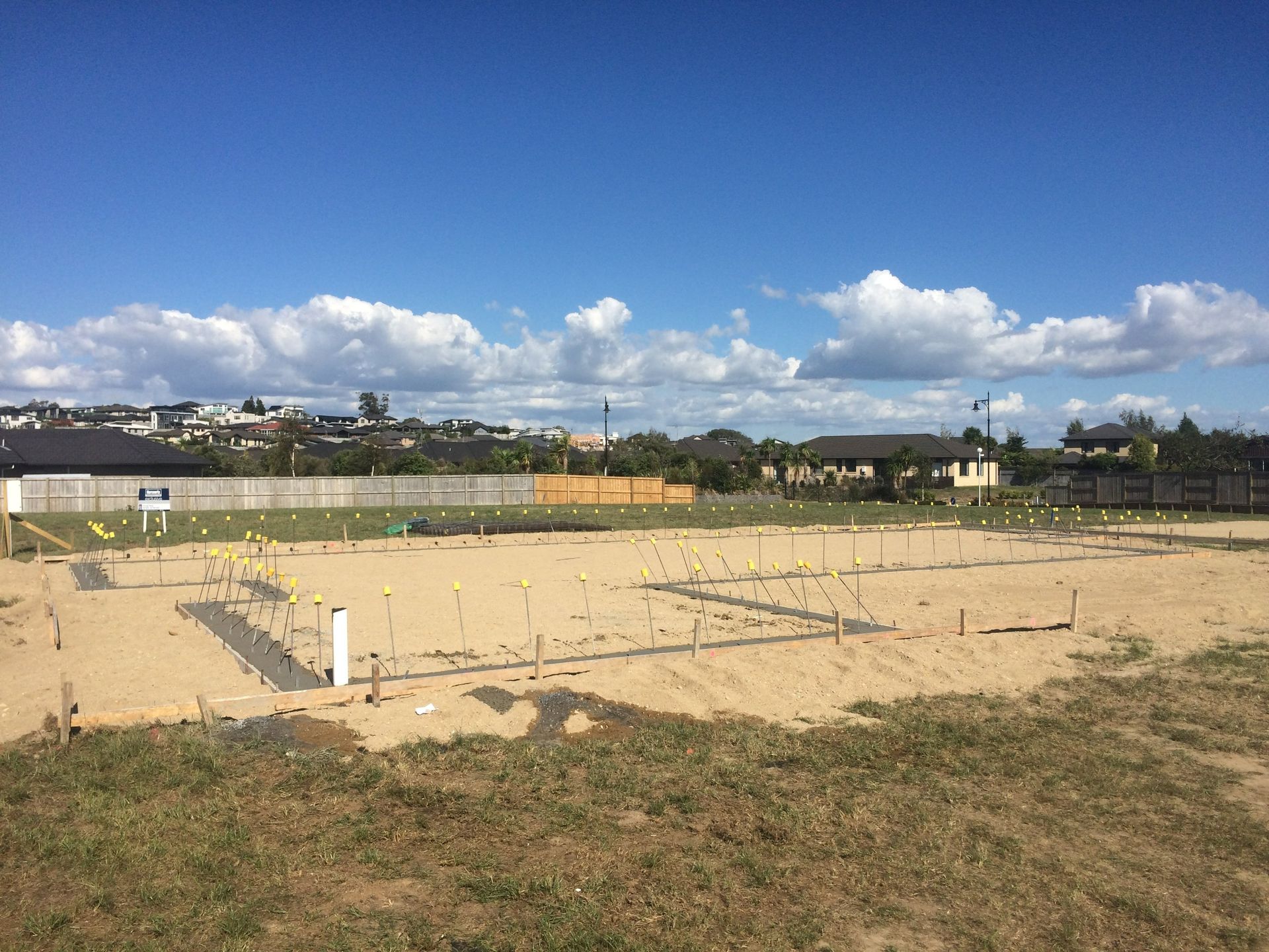 Construction site, cleared dirt, marked foundation outlines, sunny day.