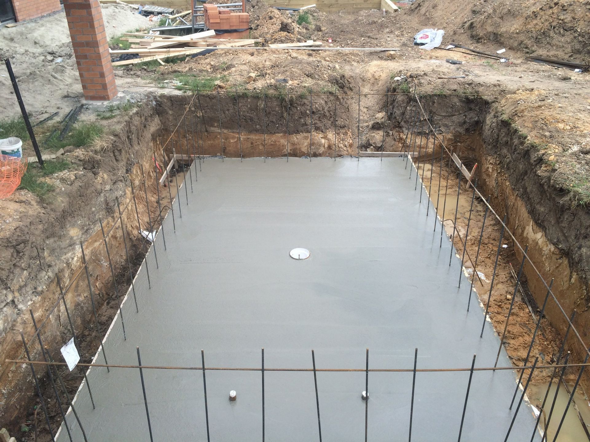 Concrete foundation poured in a rectangular excavation, with rebar extending from the edges.