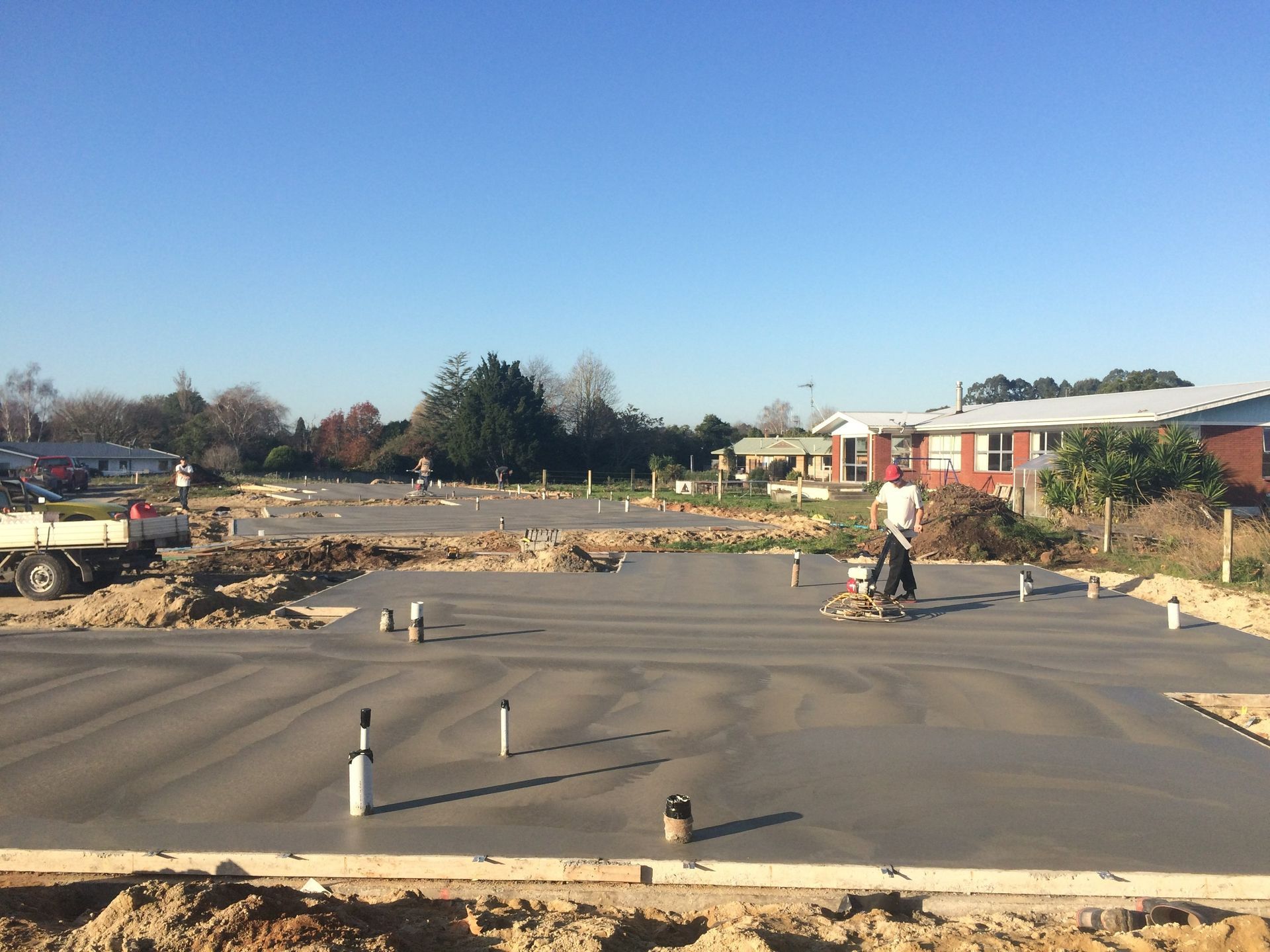 Freshly poured concrete foundation at a construction site, with workers in the distance.