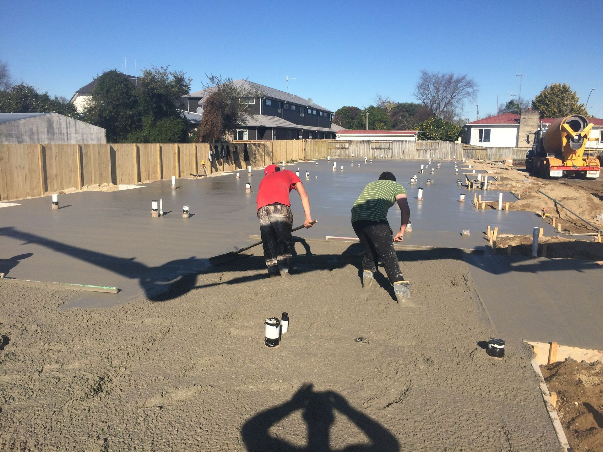 Two workers smoothing wet concrete foundation at construction site.