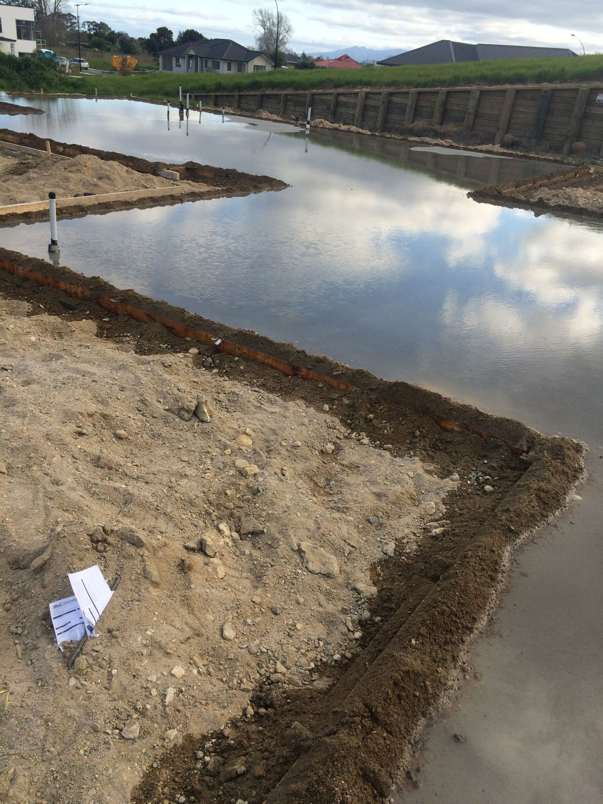 Flooded construction site with exposed soil and water reflecting the sky.