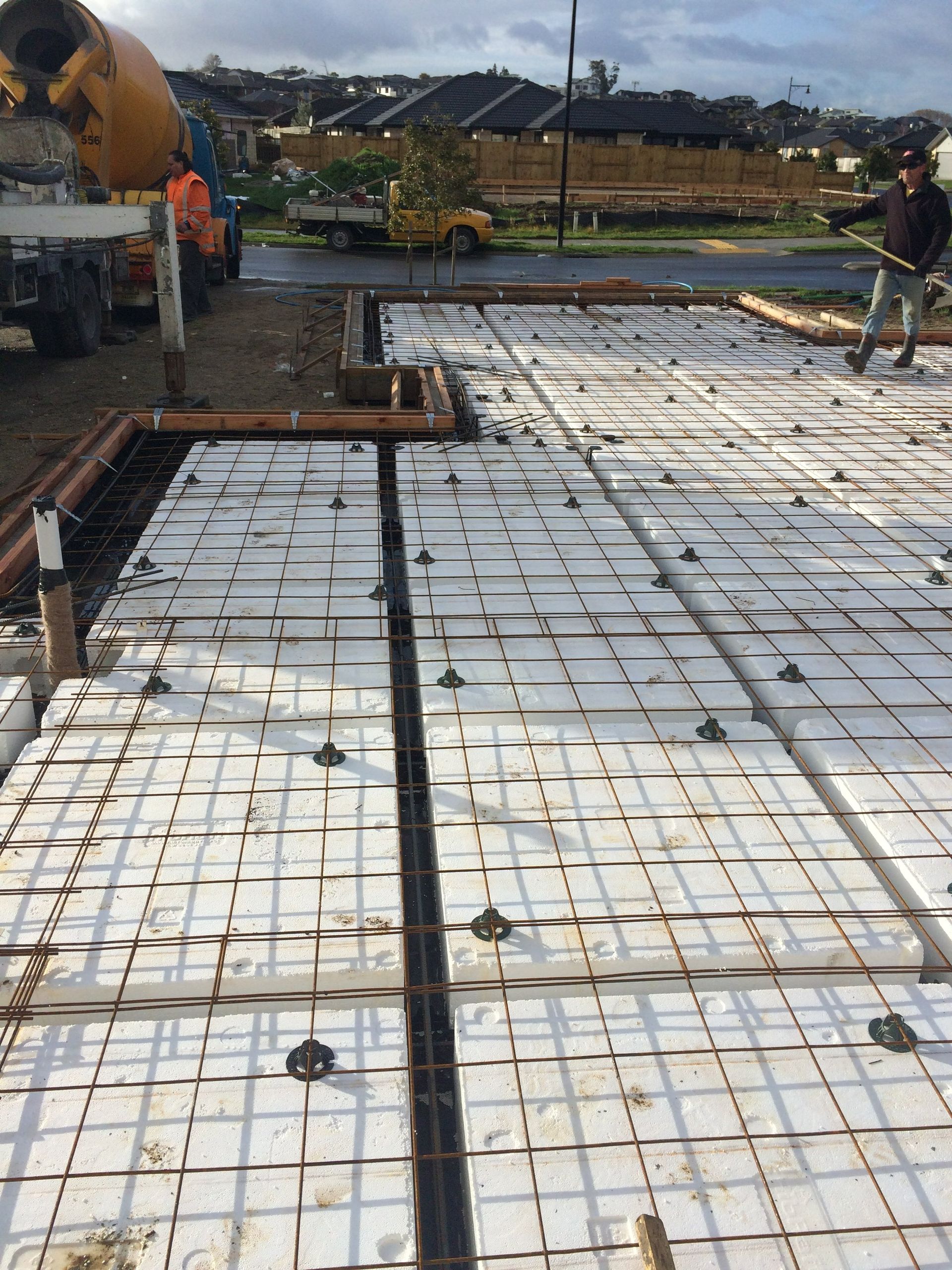Construction site: concrete foundation with foam blocks, rebar, and workers in action.